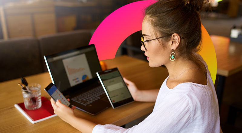 Woman sits infront of laptop holding a mobile phone and tablet