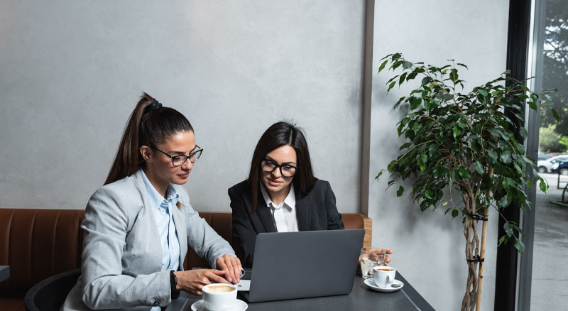 Two employees collaborate in a cafe using a laptop
