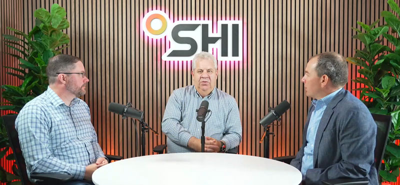 Three men holding a discussion infront of the SHI logo