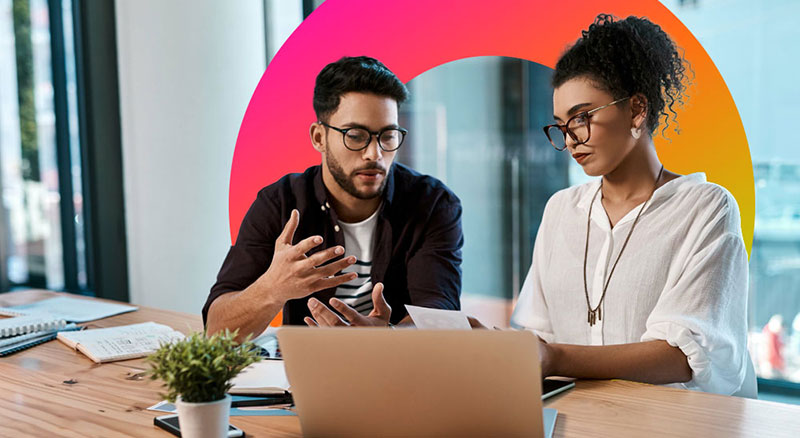 Two employees discuss information behind a laptop