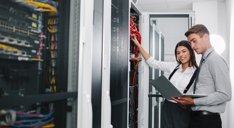 Two professionals examining a server rack in a data center with a binder in their hands.