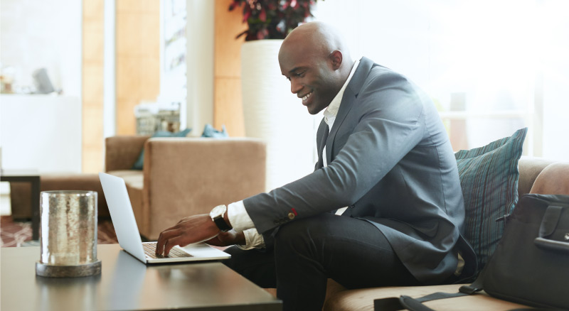 A formally dressed individual using a laptop on a coffee table in an elegant living room with a vase and a bag