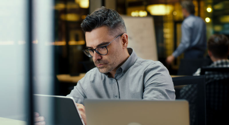 A person working on a laptop in a modern office with colleagues in the background