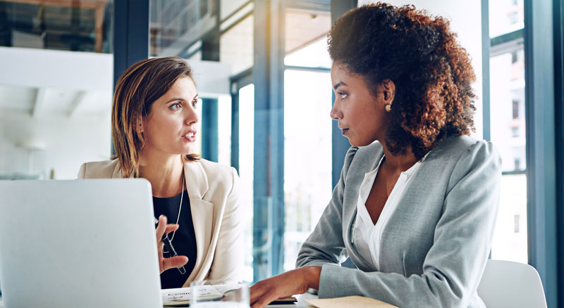 Two professionals having a discussion in front of a laptop in an office setting