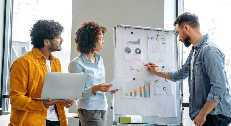 Three people discussing data and graphs on a whiteboard