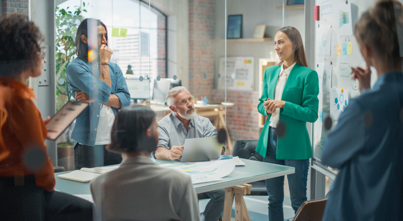 A team of professionals in a meeting room discussing ideas and strategies, surrounded by charts and diagrams.