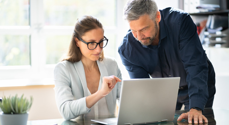 Two professionals discussing work on a laptop in a bright office environment.