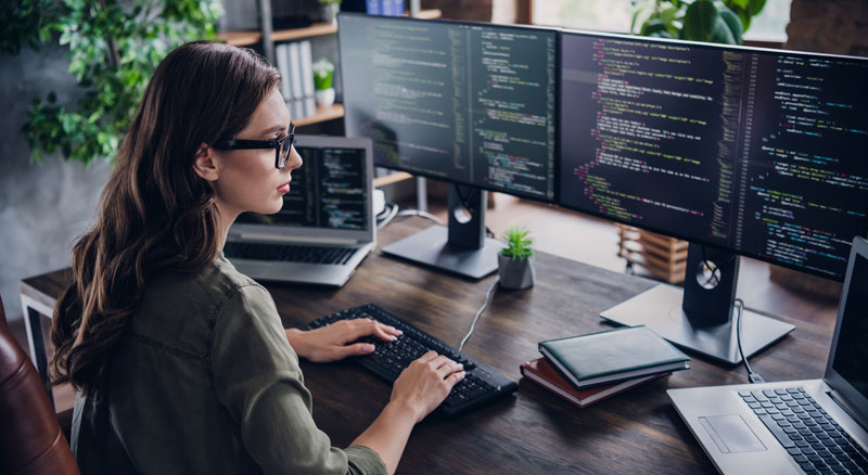 A person coding on a computer with multiple monitors