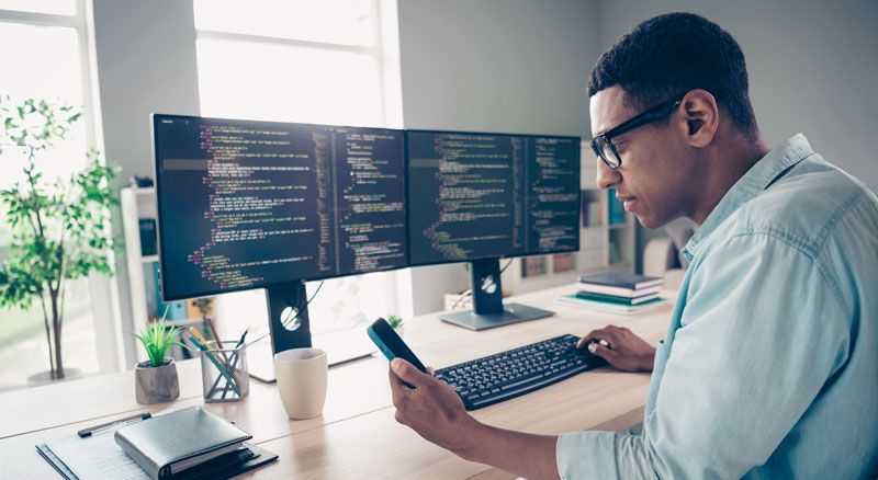 A person working on code at a multi-monitor setup