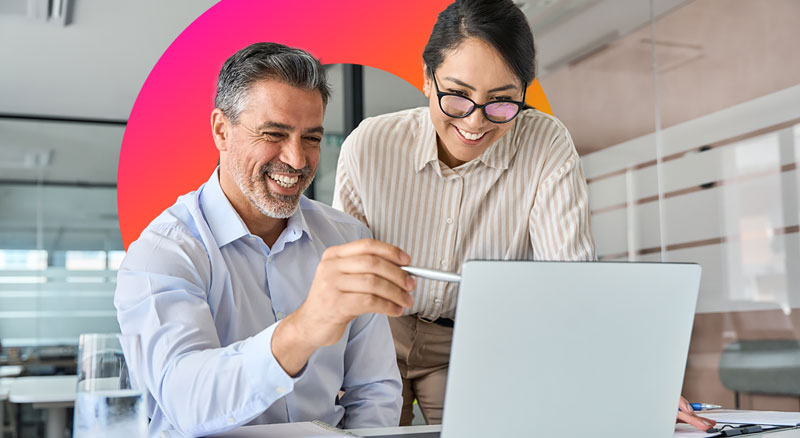 Two individuals in a modern office setting, engaging in a discussion while looking at a laptop