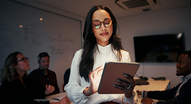 A person holding a tablet standing infront of an office meeting