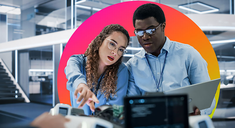 Two coworkers use a laptop while reviewing information in a bright office