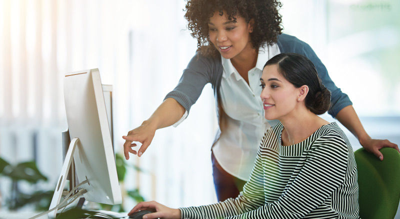 Two individuals working together at a computer in an office setting