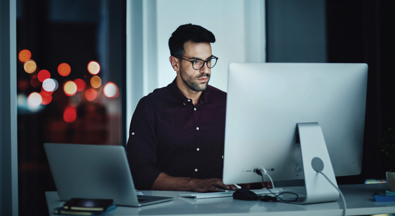 Person working on computer in dark room with city view