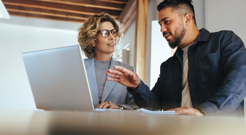 Two individuals discussing a document in front of a laptop
