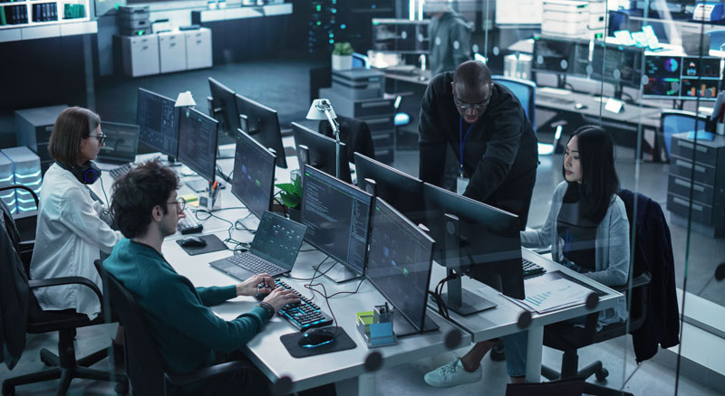 A group of professionals working at a well-equipped office with multiple computer monitors displaying data