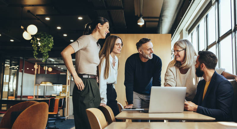 A group of five individuals are focused on a laptop in a modern, well-lit office environment