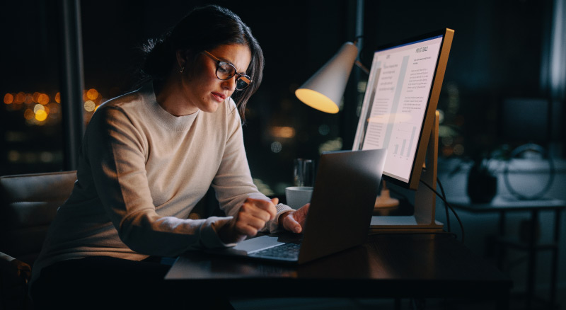 An individual is working at a desk with multiple computers, one of which displays lines of code, while the others show graphical data and charts