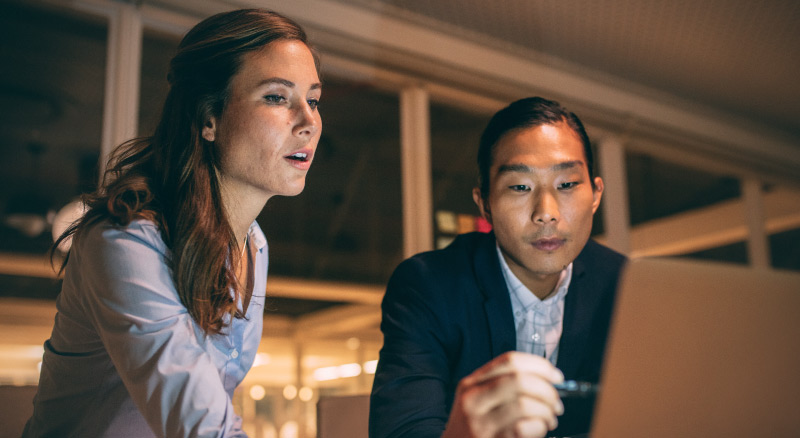 Two people are focused on a laptop, engaged in a discussion or collaborative work in an indoor setting