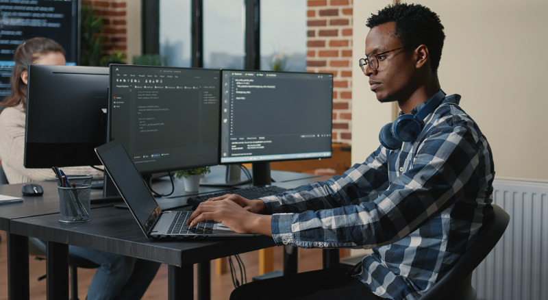 Man working on a laptop with two desktops