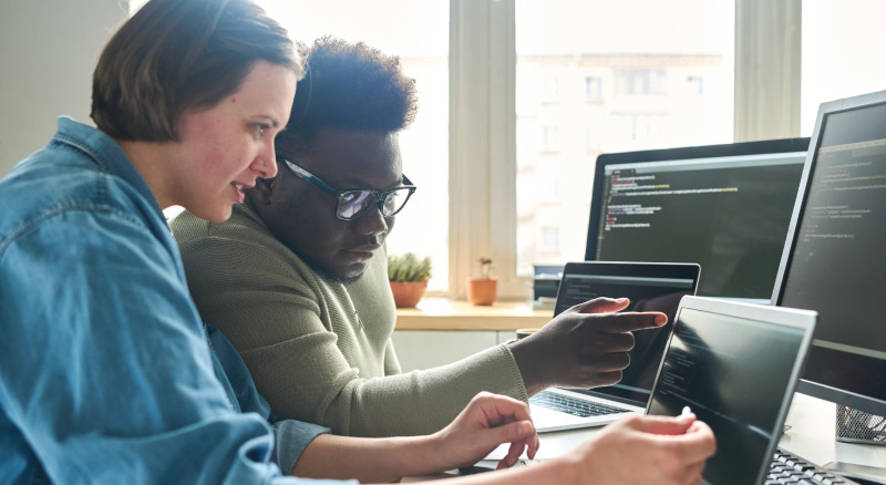 Two people working on computers near a window with code and plants