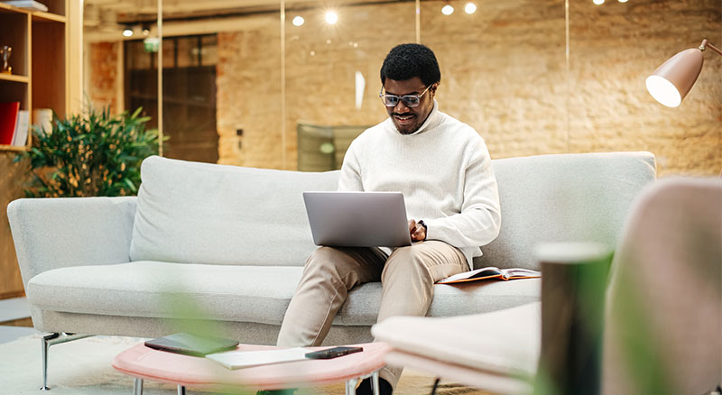 An individual seated on a couch, engrossed in laptop work.