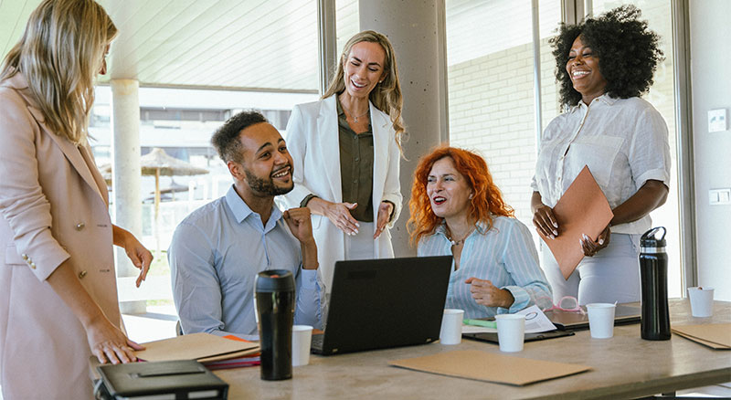 A diverse group of individuals huddled around a laptop, engrossed in a shared activity.