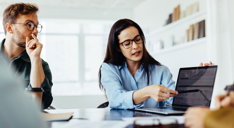 Woman reviews reports on laptop with another employee