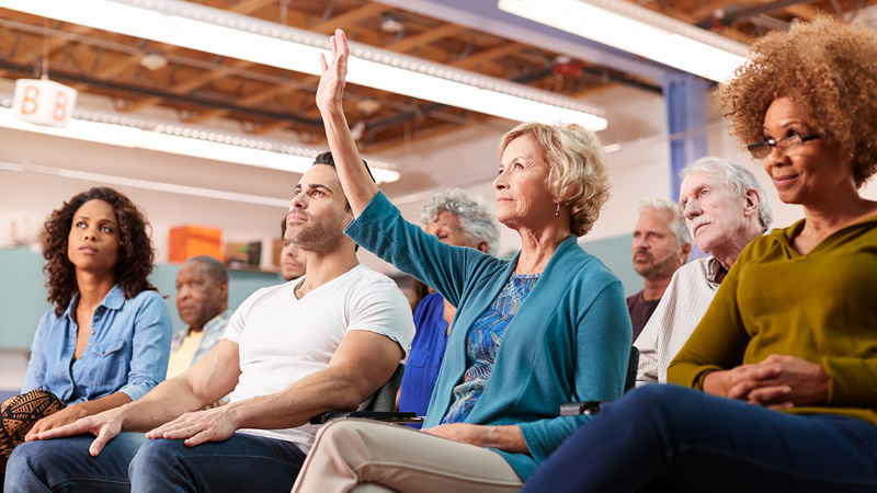 Woman in an audience raises her hand during public meeting