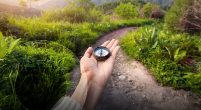 A hand holding a compass, guiding the way along a natural path surrounded by greenery and trees