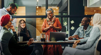 A group of people is engaged in a discussion around a table with laptops in a collaborative atmosphere