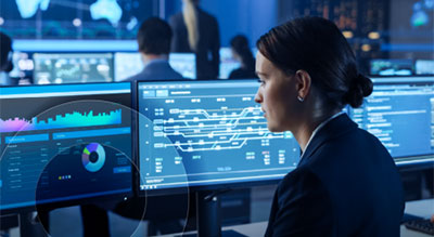 A professional monitoring multiple large screens displaying digital dashboards and data visualizations in a technology operations center