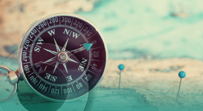 A compass placed on a map, surrounded by colorful pins indicating various locations.