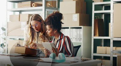 Two coworkers surrounded by boxes review inventory together