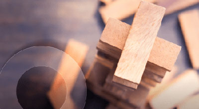 A close-up image of wooden blocks stacked in a precarious tower, with some blocks removed, indicating a game of skill and balance