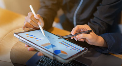 Two people reviewing charts and graphs on a tablet, analyzing data with a stylus and pen