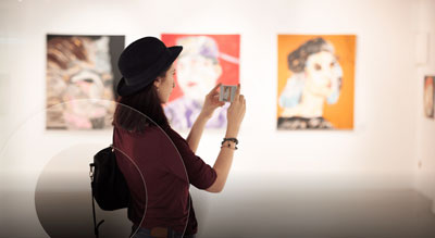 A person in an art gallery, taking a photo of artwork with their smartphone