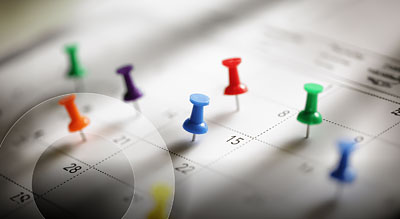 A close-up of a calendar with multiple colorful push pins marking specific dates, indicating important events