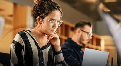 A woman with glasses and a male coworker looking at their laptops working on building a cloud environment using aws