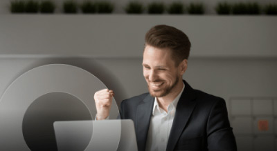 A man celebrating with his fist up in mid air sitting behind a laptop