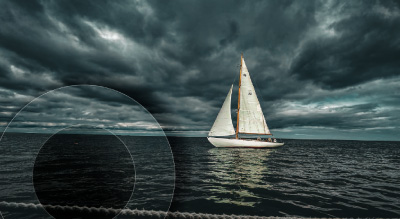 A white sailboat glides on dark, choppy waters under a cloudy, overcast sky