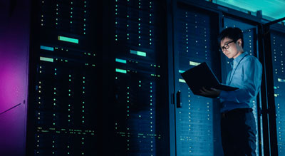 Person holding a laptop in front of a blue-lit server room