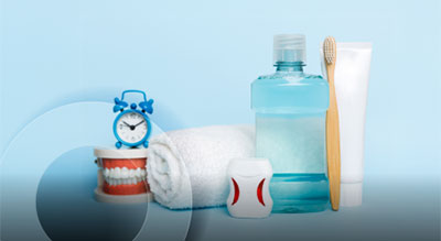 Dental hygiene items including a toothbrush, toothpaste, mouthwash, dental floss, a rolled towel, and a model of teeth with a small clock, arranged against a light blue background