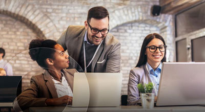 Three coworkers collaborate behind two laptops in an office environment