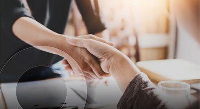 Two people shaking hands over a table with papers and a cup of coffee, symbolizing agreement or partnership