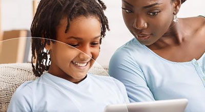 A child and an adult sitting on a couch and using a laptop