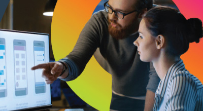 Two people collaborate at a computer, reviewing a mobile app design on the screen.