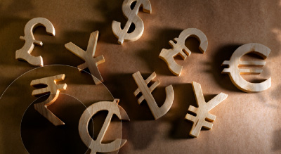  Wooden currency symbols for the euro, dollar, yen, pound, and rupee scattered on a brown surface