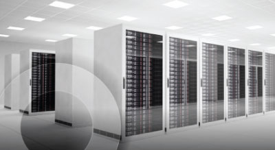 A row of tall, black server racks in a data center with a white floor, walls, and ceiling illuminated by fluorescent lights