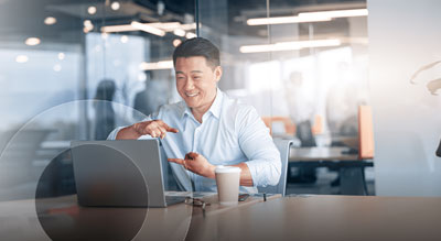 A person working on a laptop at a table with a coffee cup beside them, in a bright office setting